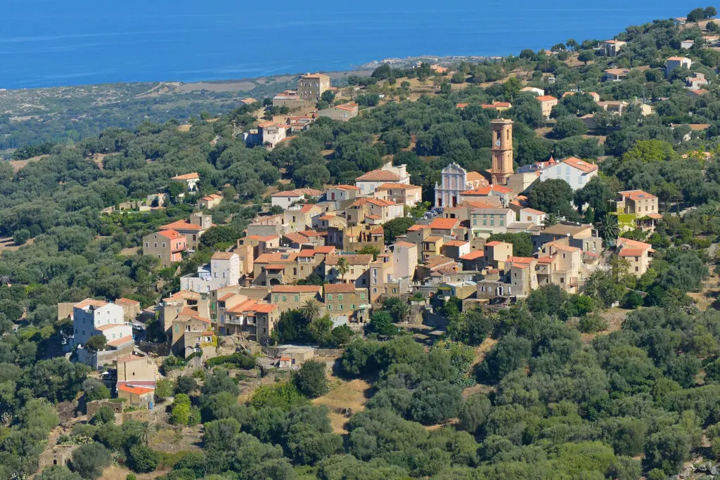 vue-aerienne-dun-village-corse-en-bord-de-mer Vue pittoresque d'un village corse face à la mer, entouré de végétation luxuriante et baigné de soleil, idéal pour découvrir les charmes méditerranéens.