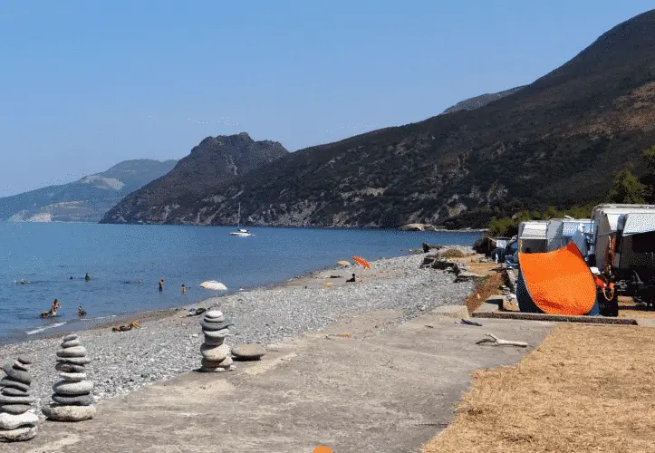 Image of a pebble beach in Corsica near Bastia, ideal for camping, with stunning views of the sea and surrounding mountains.