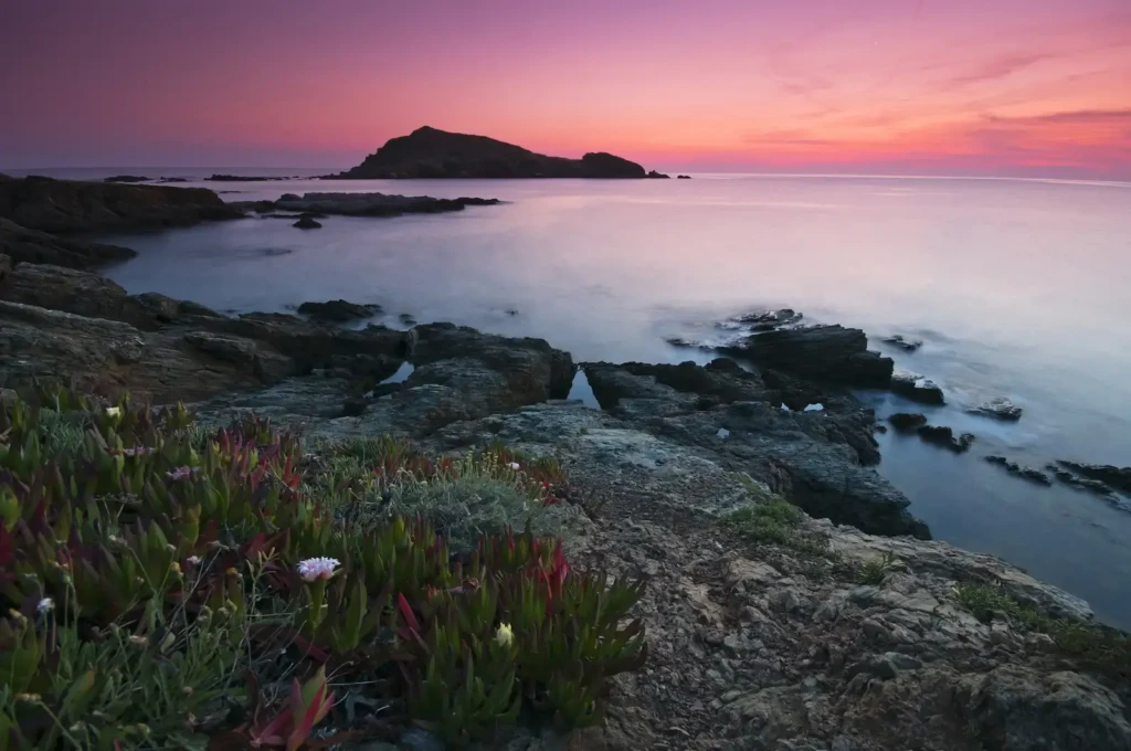 coucher-de-soleil-ilot-centuri-cap-corse Vue sur le port de pêche de Centuri dans le Cap Corse au coucher du soleil. Les rochers au premier plan et l'îlot de Centuri à l'horizon sous un ciel aux teintes roses et violettes.