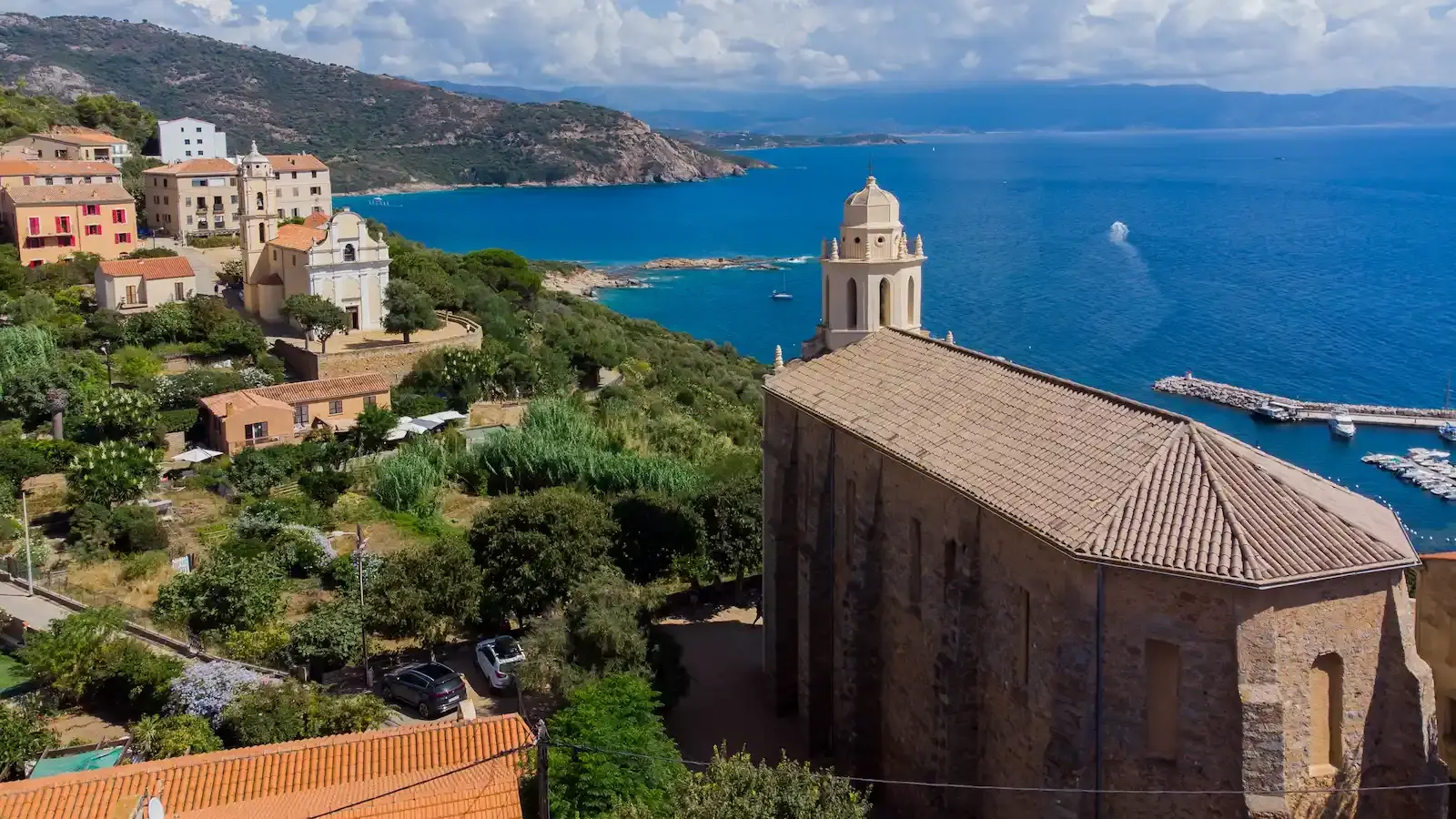 Vue panoramique sur le village de Cargèse dominant la mer Méditerranée. Au premier plan, l'église latine Saint-Spiridion faisant face au golfe de Sagone, entourée d'une végétation méditerranéenne luxuriante et de maisons villageoises.