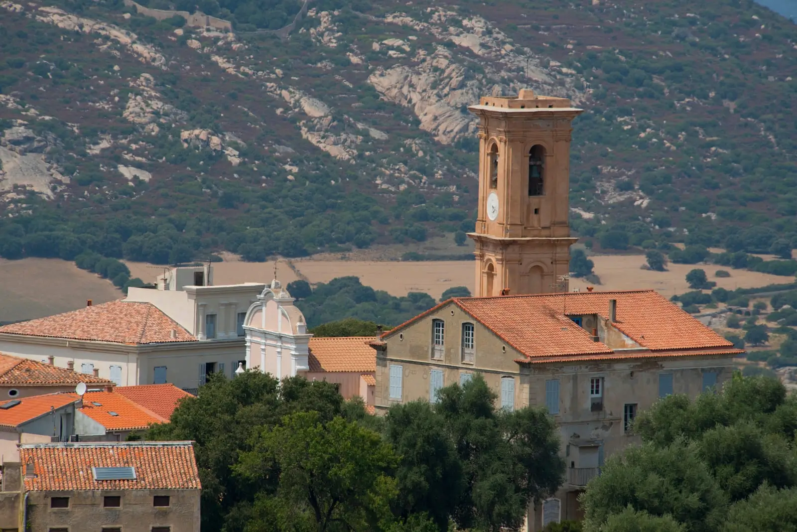 Cœur historique d’un village balanin Clocher et maisons traditionnelles d’un village de Balagne en Haute-Corse, avec collines en arrière-plan.