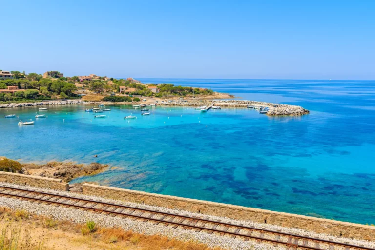 Vue d’une crique turquoise en Balagne avec petits bateaux et maisons sur les collines.