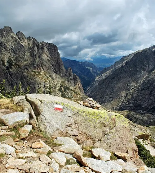 Sentier pittoresque en Corse offrant un panorama époustouflant avec des crêtes montagneuses contrastant entre roche rugueuse et verdure, incitant à l'exploration et à l'évasion dans la nature.