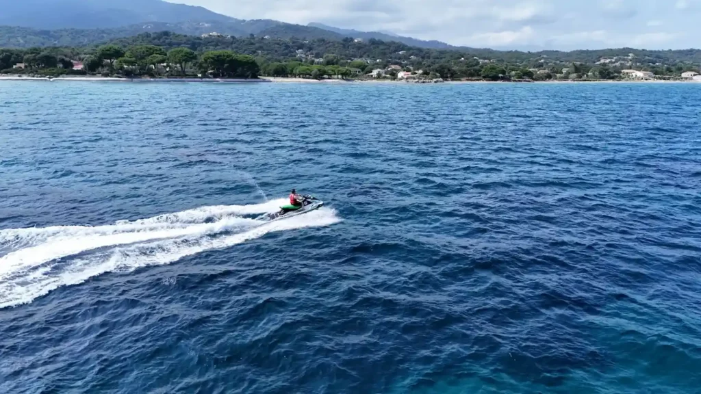 Jet-ski activité nautique en Corse pour les vacances Personne pratiquant le jet-ski en pleine mer en Corse, vue aérienne sur les eaux turquoise de la Méditerranée et le littoral sauvage.