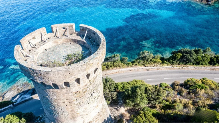 Vue aérienne d'une tour génoise historique surplombant les eaux turquoise de la côte corse.